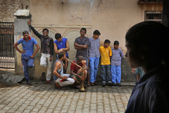 In this Aug. 13, 2015, photo, village boys stand and smoke in an alley as girl walks past in Sorkhi village, 150 kilometers (93 miles) west of New Delhi, in the northern Indian state of Haryana. Haryana's shortage of brides is the direct consequence of the skewed gender ratio in the state, due to sex-selective abortions in a society where many families prize boys over girls, mostly for economic reasons.  (AP Photo/Manish Swarup)